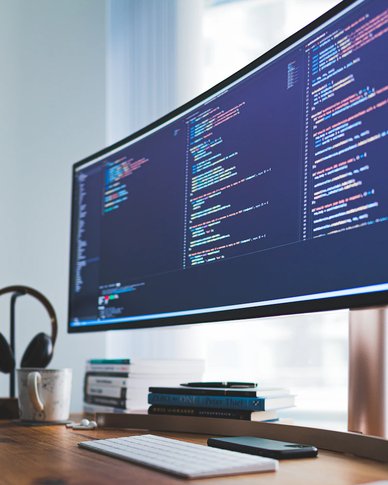 A bright software development workspace with code on a monitor above a wooden desk.